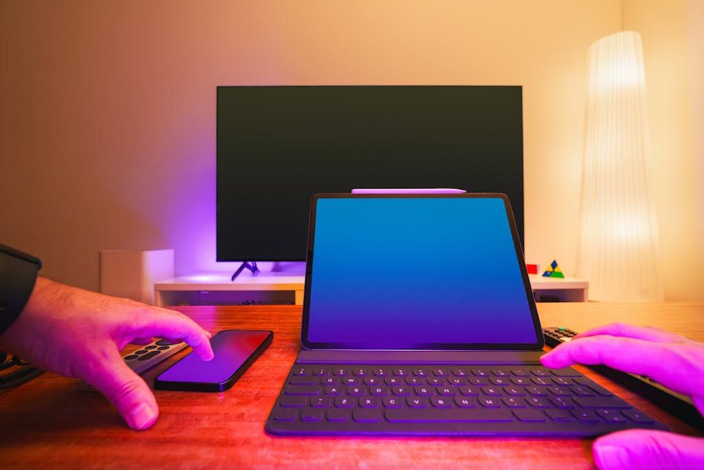 A vibrant workspace featuring a laptop, tablet, and TV with colorful lighting.